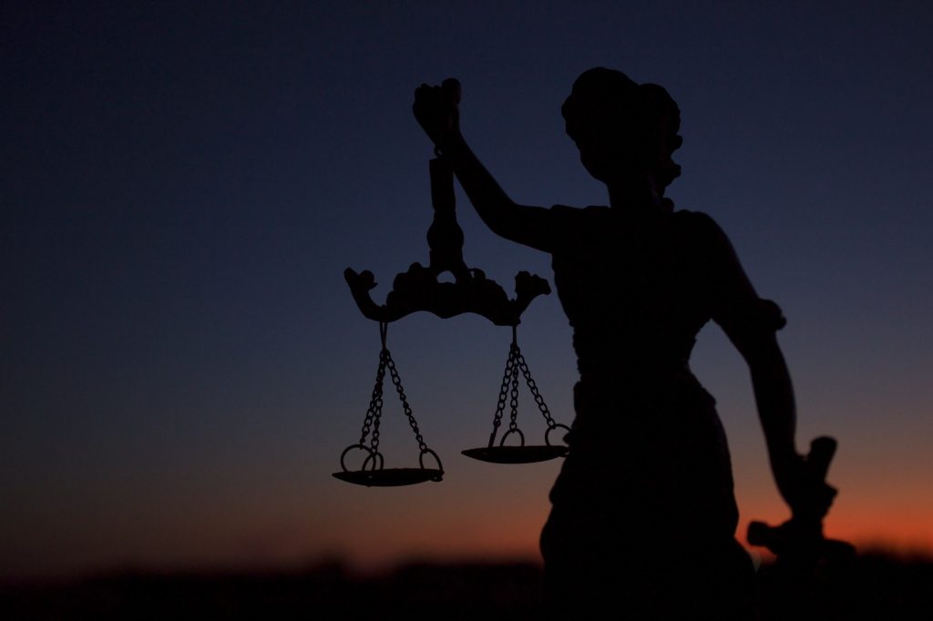dark silhouette of the statue of Themis - the goddess of justice, against the background of a red su