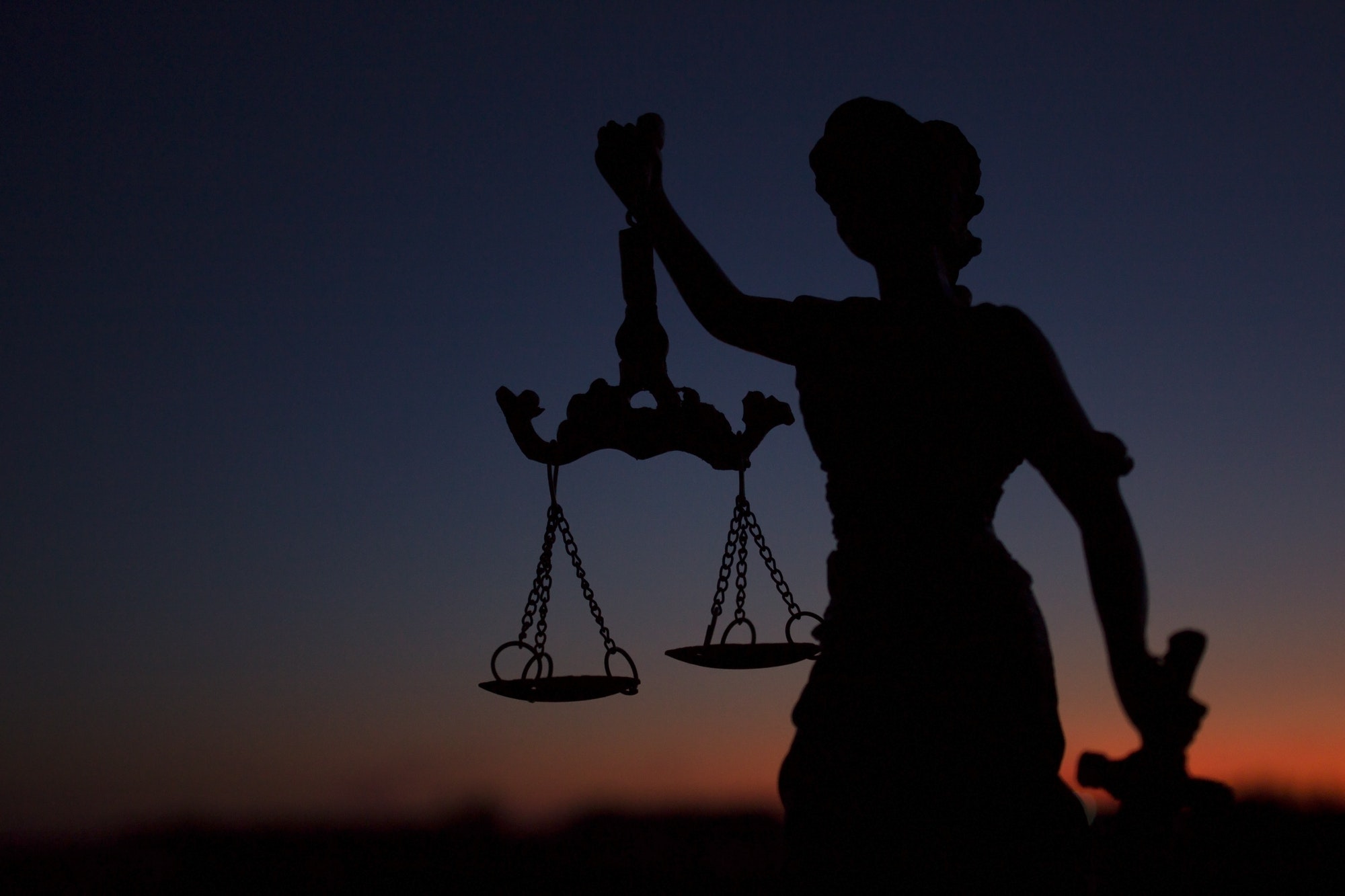 dark silhouette of the statue of Themis - the goddess of justice, against the background of a red su